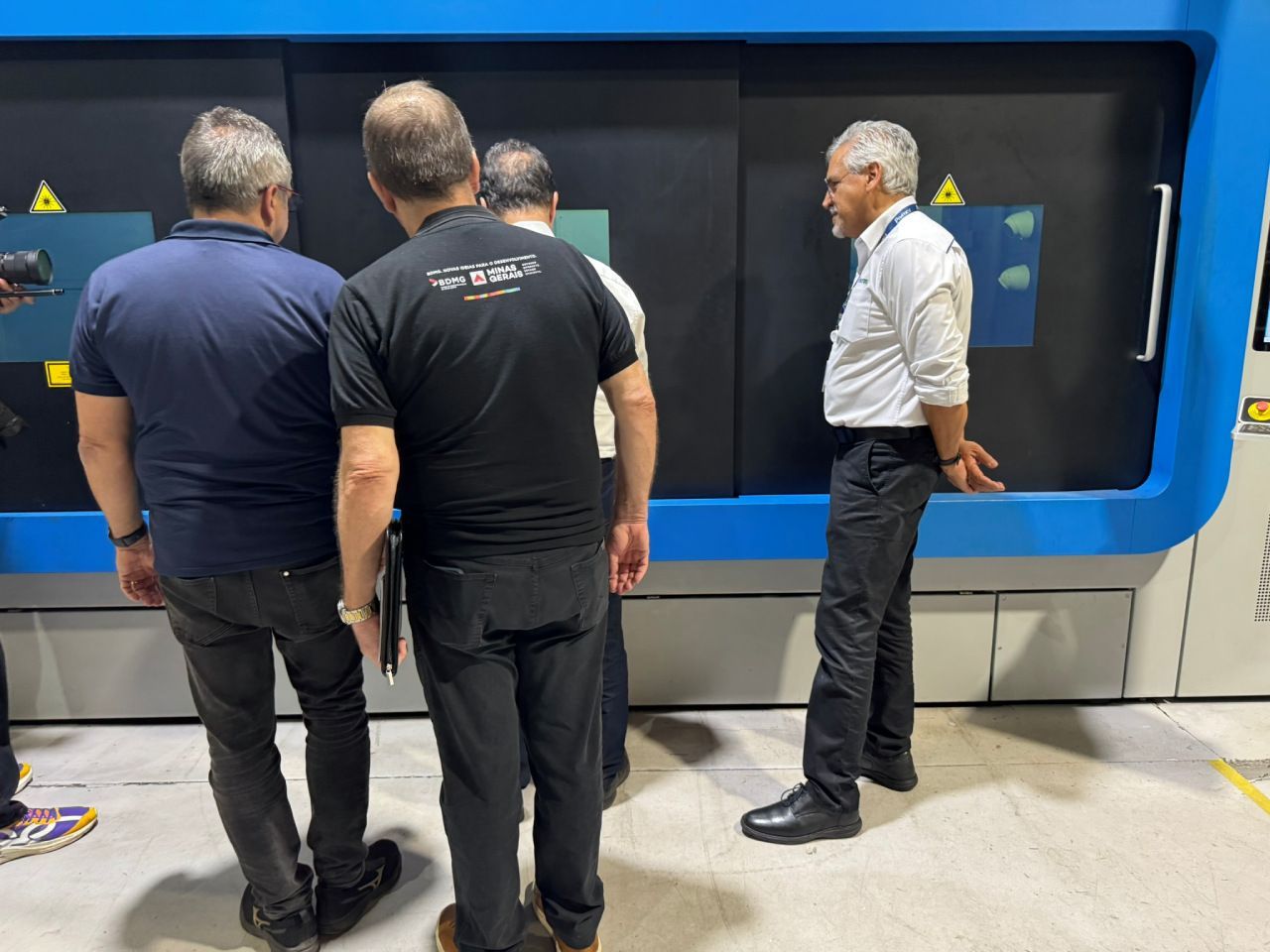 Um grupo de homens está em pé na frente de uma máquina olhando para ela.