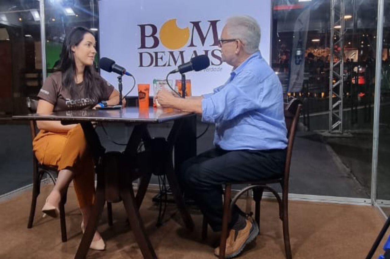 Um homem e uma mulher estão sentados à mesa conversando em microfones.