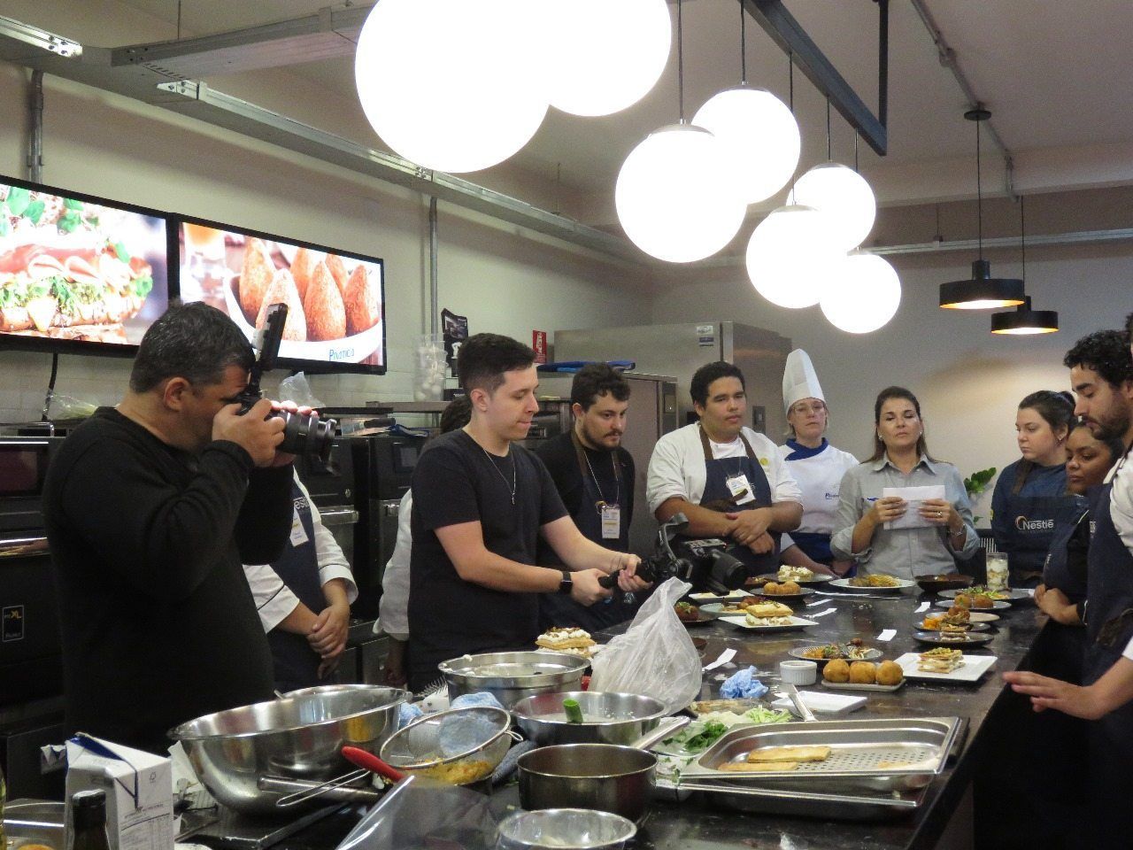 Um grupo de pessoas está em pé ao redor de uma mesa na cozinha.