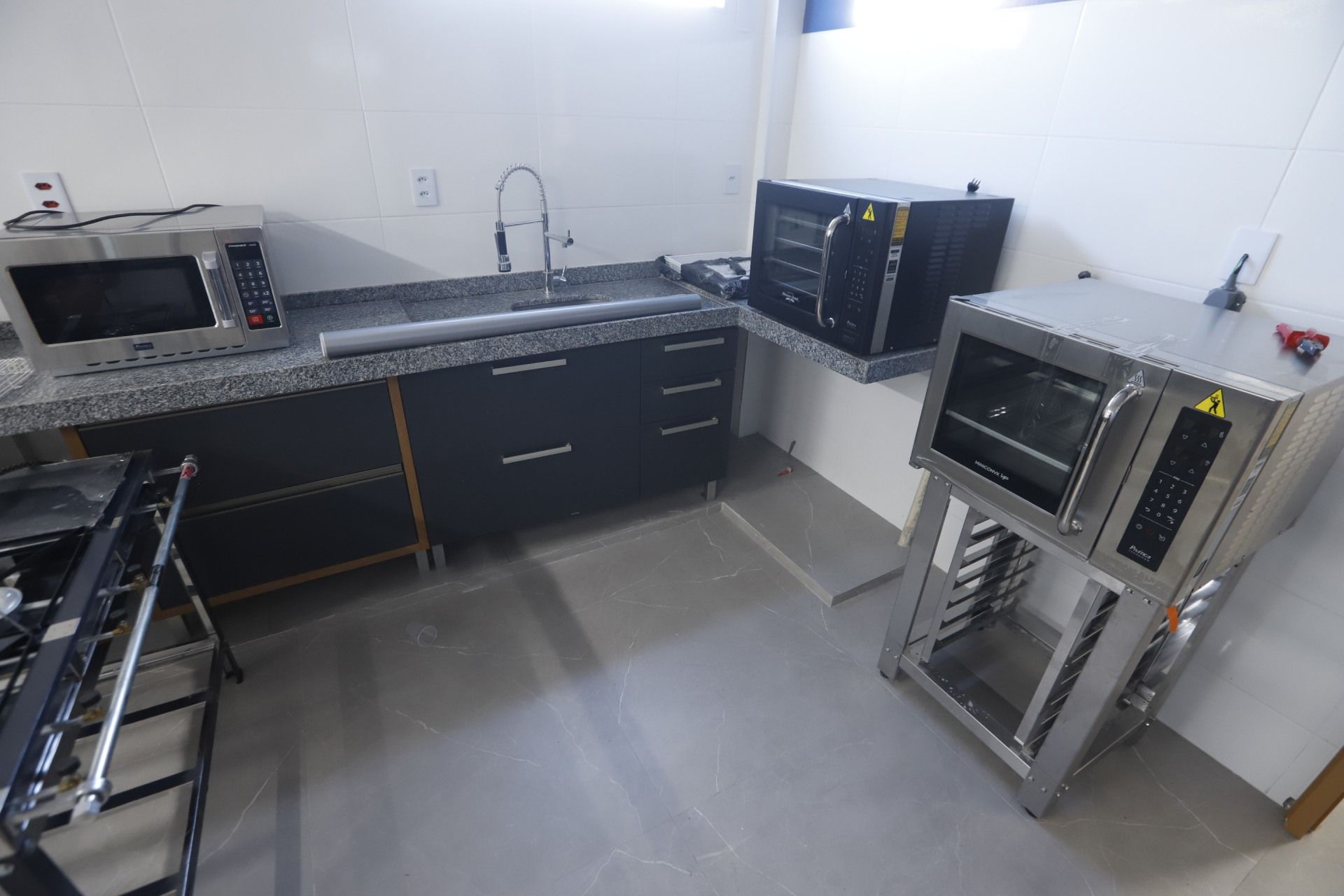 Cozinha comercial com fornos de aço inoxidável, armários pretos e bancada cinza.