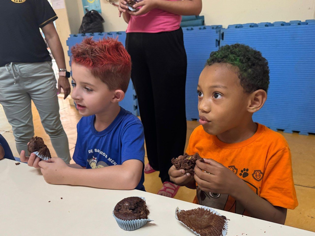 Dois meninos estão sentados à mesa comendo cupcakes de chocolate