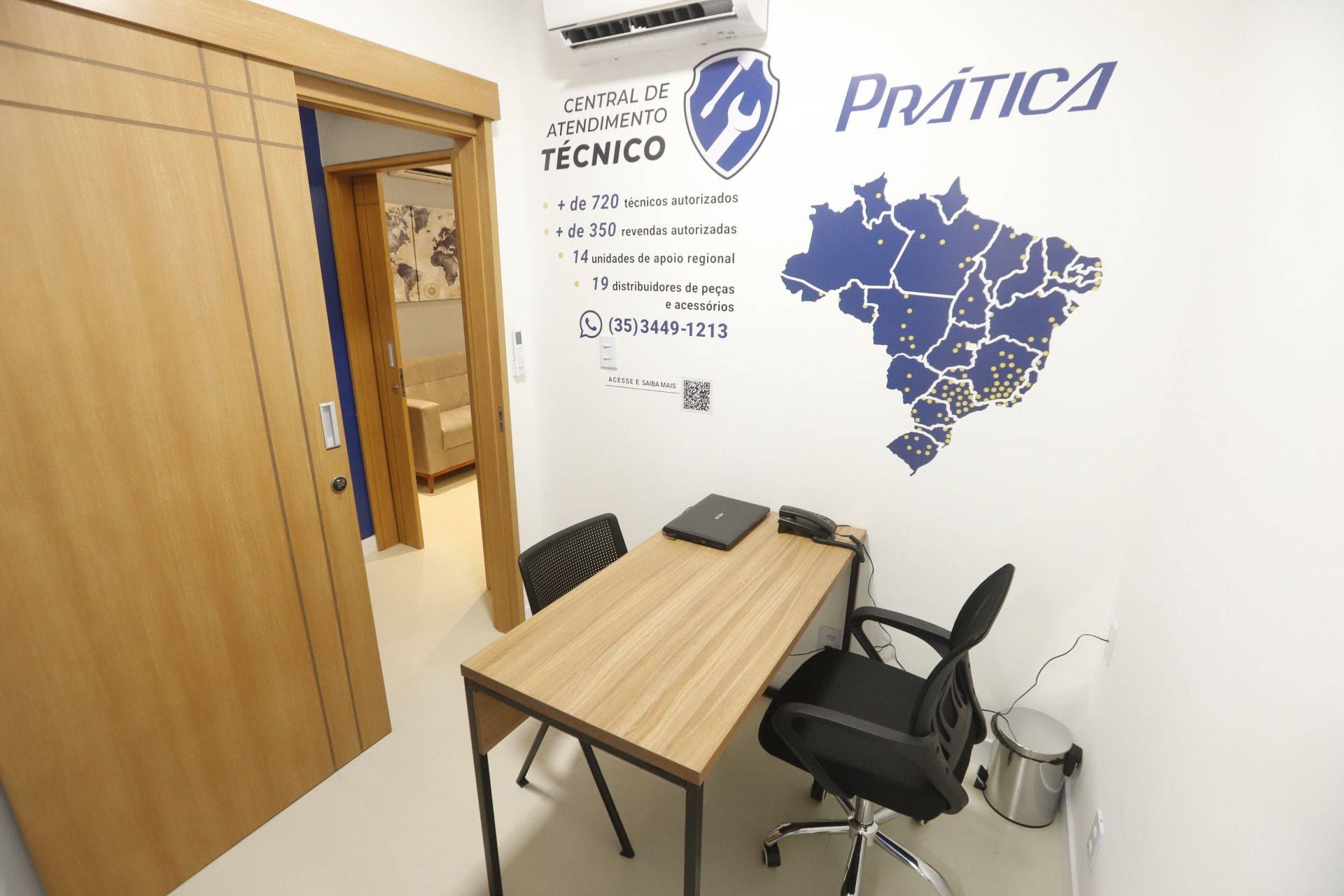 Pequeno escritório com mesa, duas cadeiras e uma parede com mapa do Brasil e logotipo da empresa.