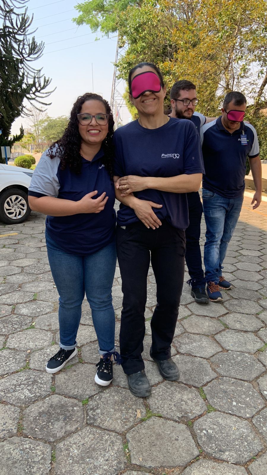 Um grupo de pessoas com os olhos vendados estão de pé, lado a lado, na calçada.