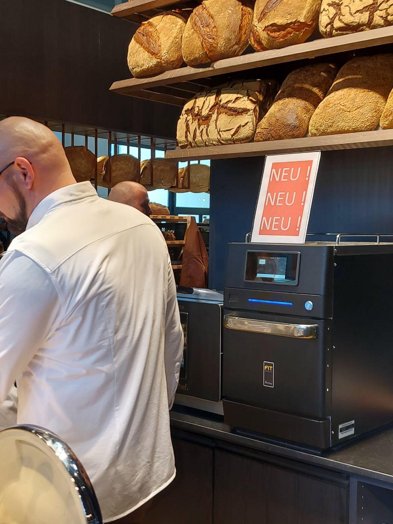Um homem de camisa branca está olhando para uma máquina em uma padaria