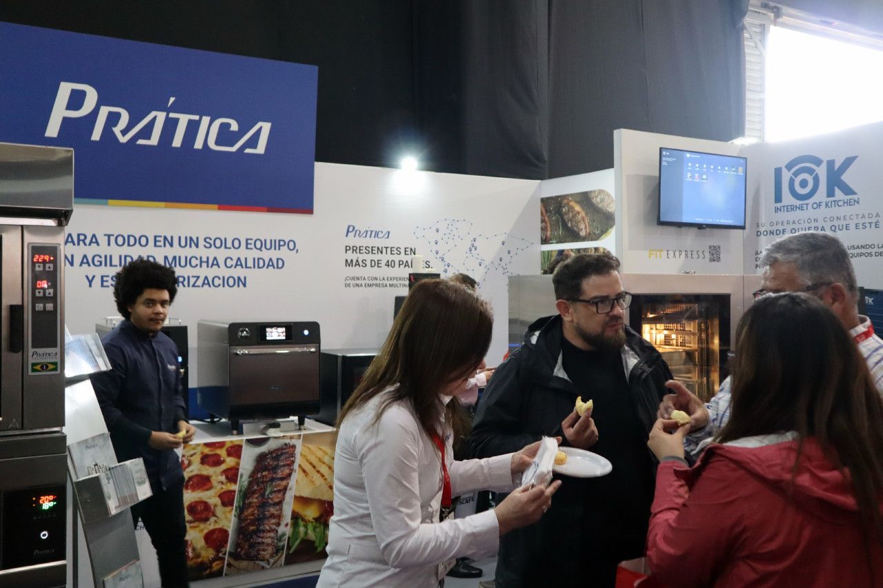 Um grupo de pessoas está em pé ao redor de uma mesa comendo.