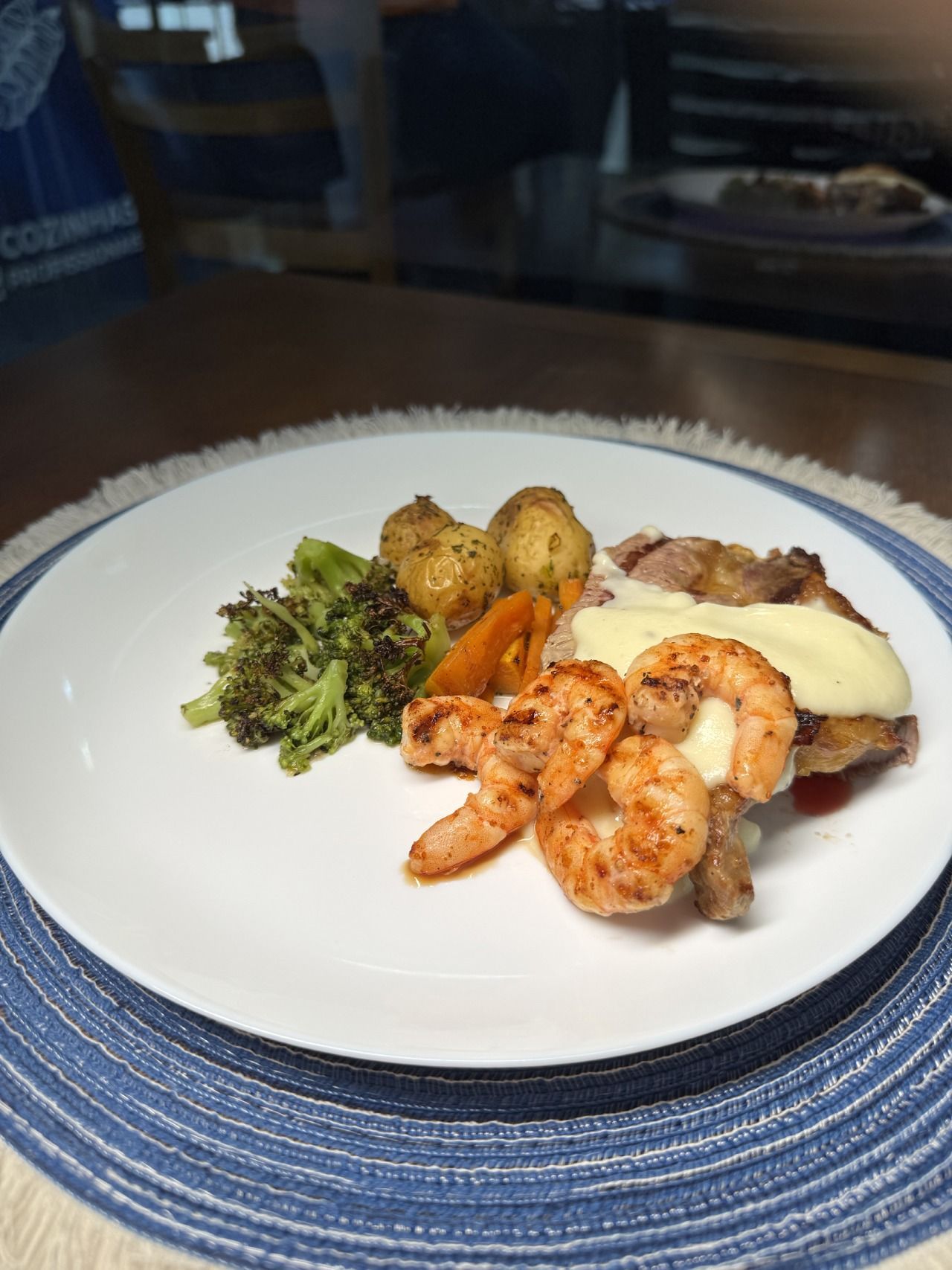 Um prato branco coberto com camarão, batatas e brócolis sobre uma mesa.