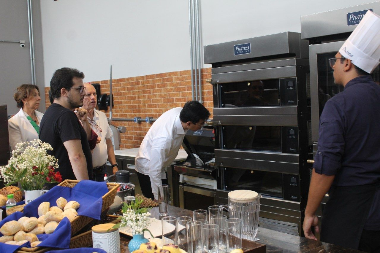 Um homem com chapéu de chef está parado em frente a um forno.