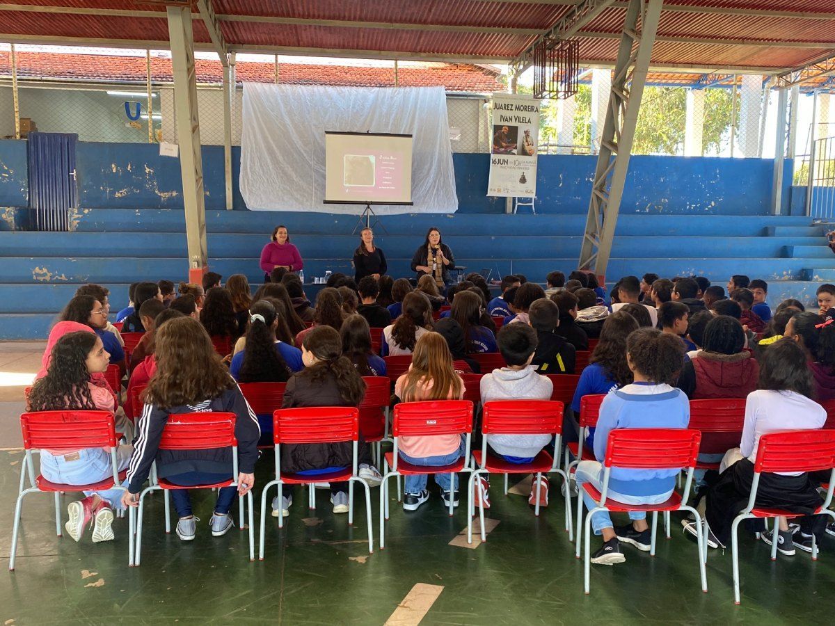 Um grupo de crianças está sentado em cadeiras vermelhas em frente a uma tela de projetor.