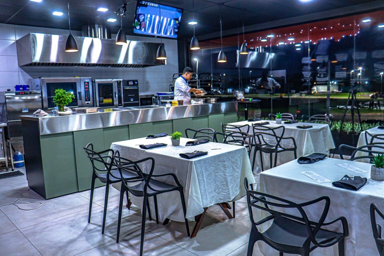 Um restaurante com mesas e cadeiras e um chef na cozinha.