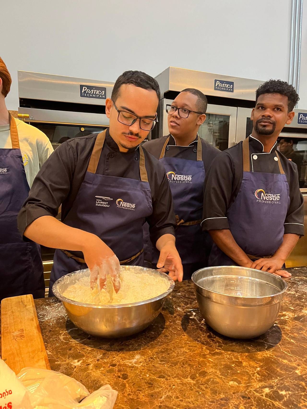 Um grupo de homens de avental estão preparando comida em uma cozinha.