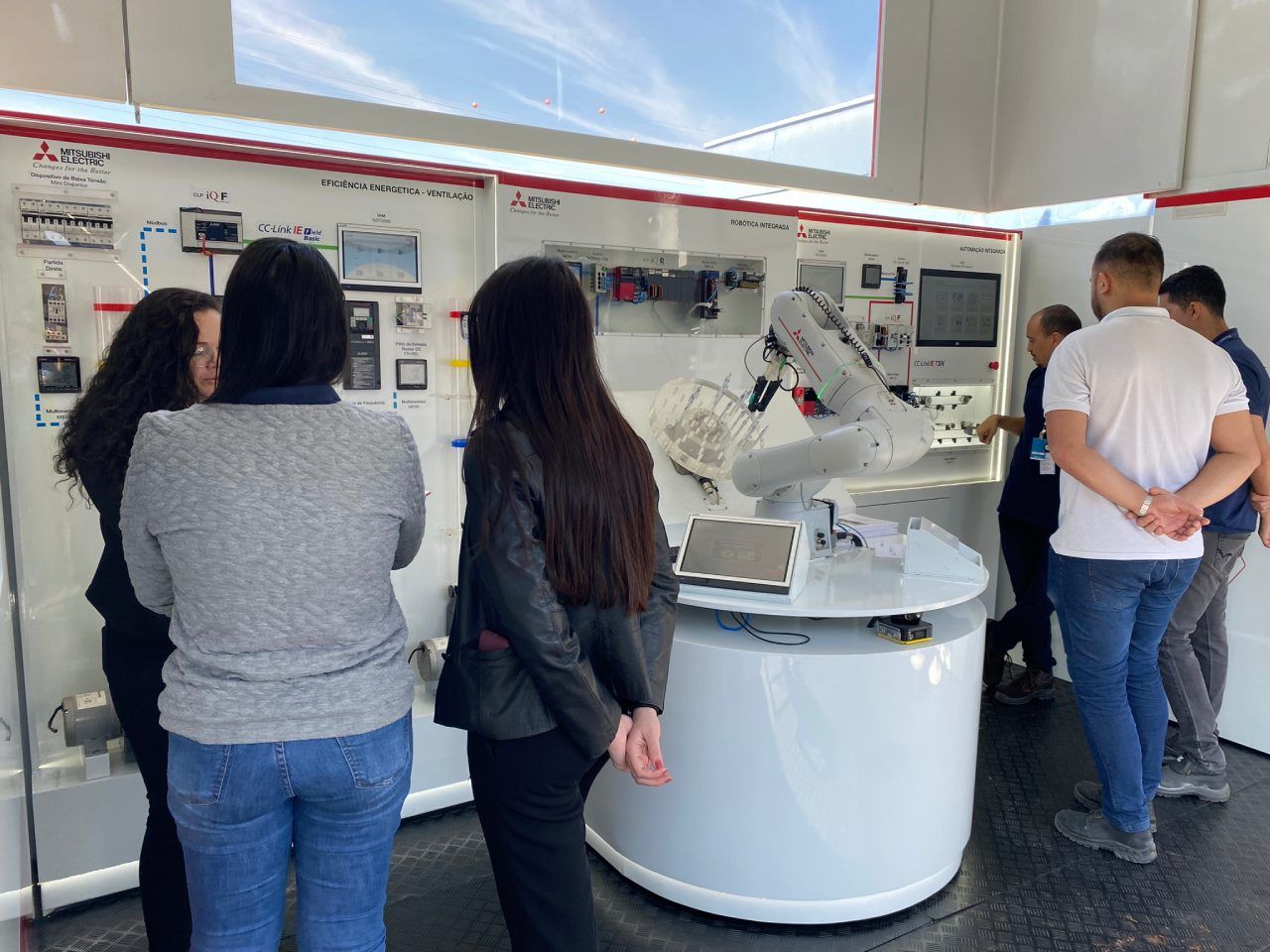 Um grupo de pessoas está em pé ao redor de uma mesa em uma sala olhando para um robô.