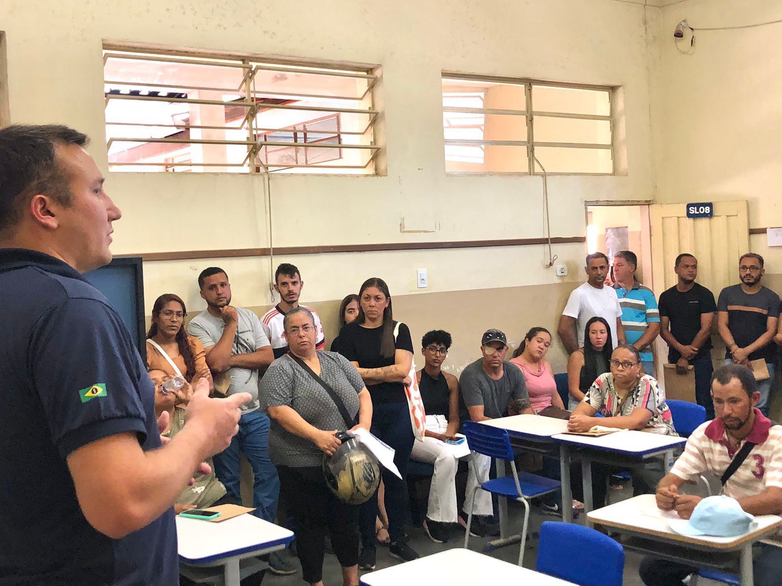 Um homem está de pé na frente de um grupo de pessoas sentadas em carteiras em uma sala de aula.