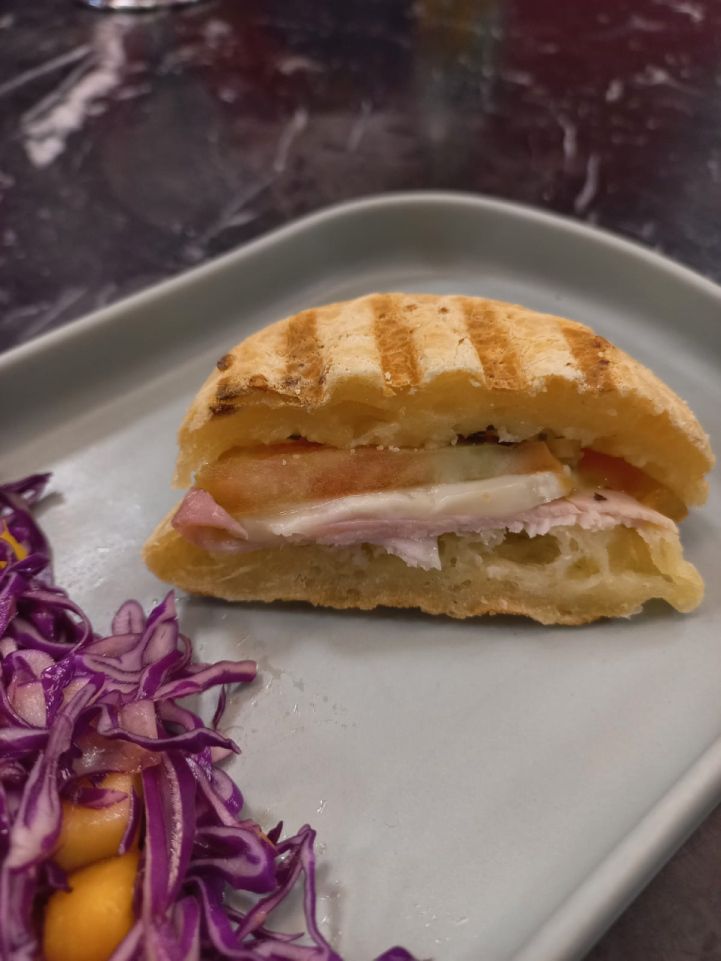 Um close de um sanduíche em um prato com salada de repolho.