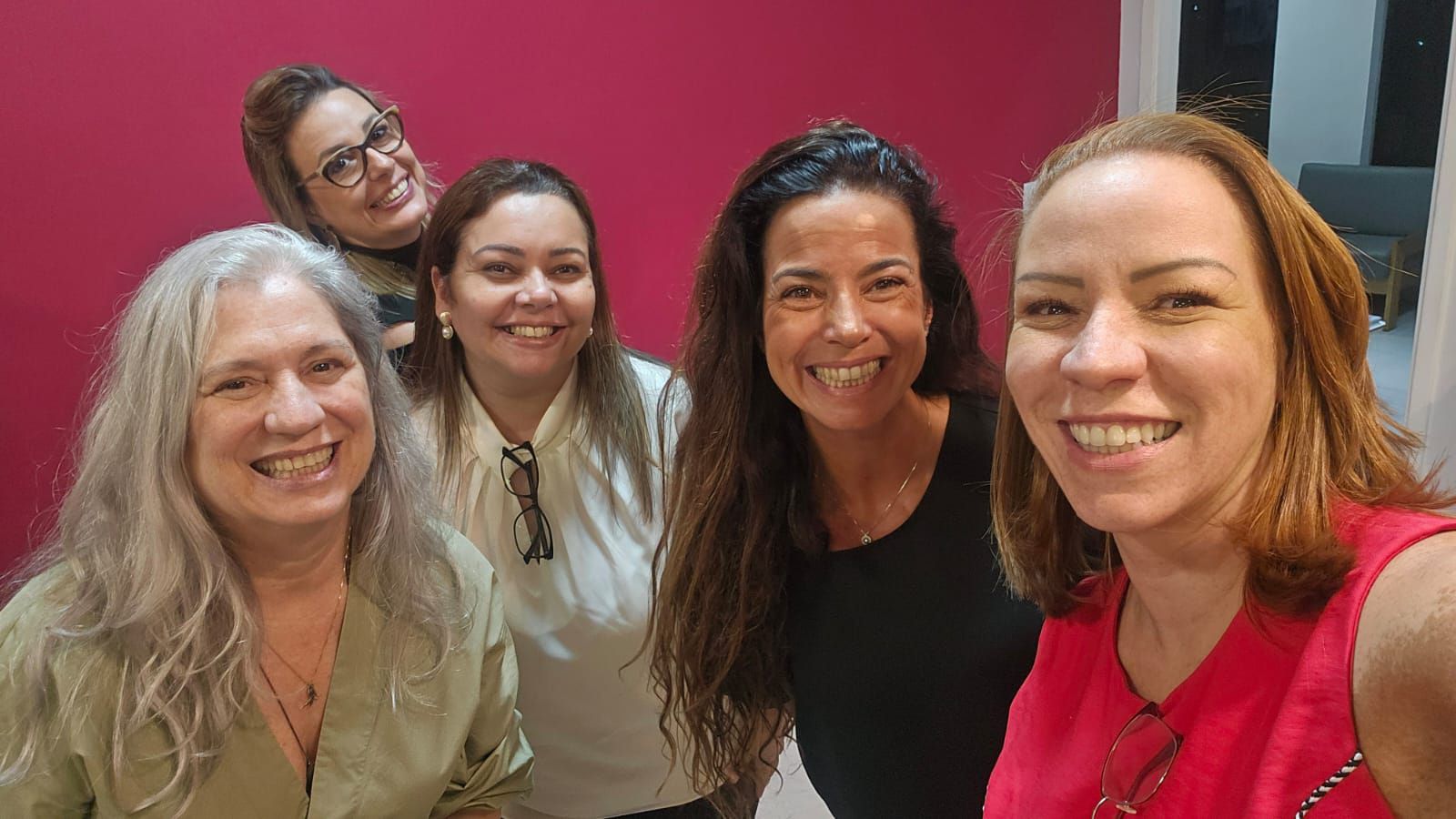 Um grupo de mulheres está posando para uma foto em frente a uma parede rosa.
