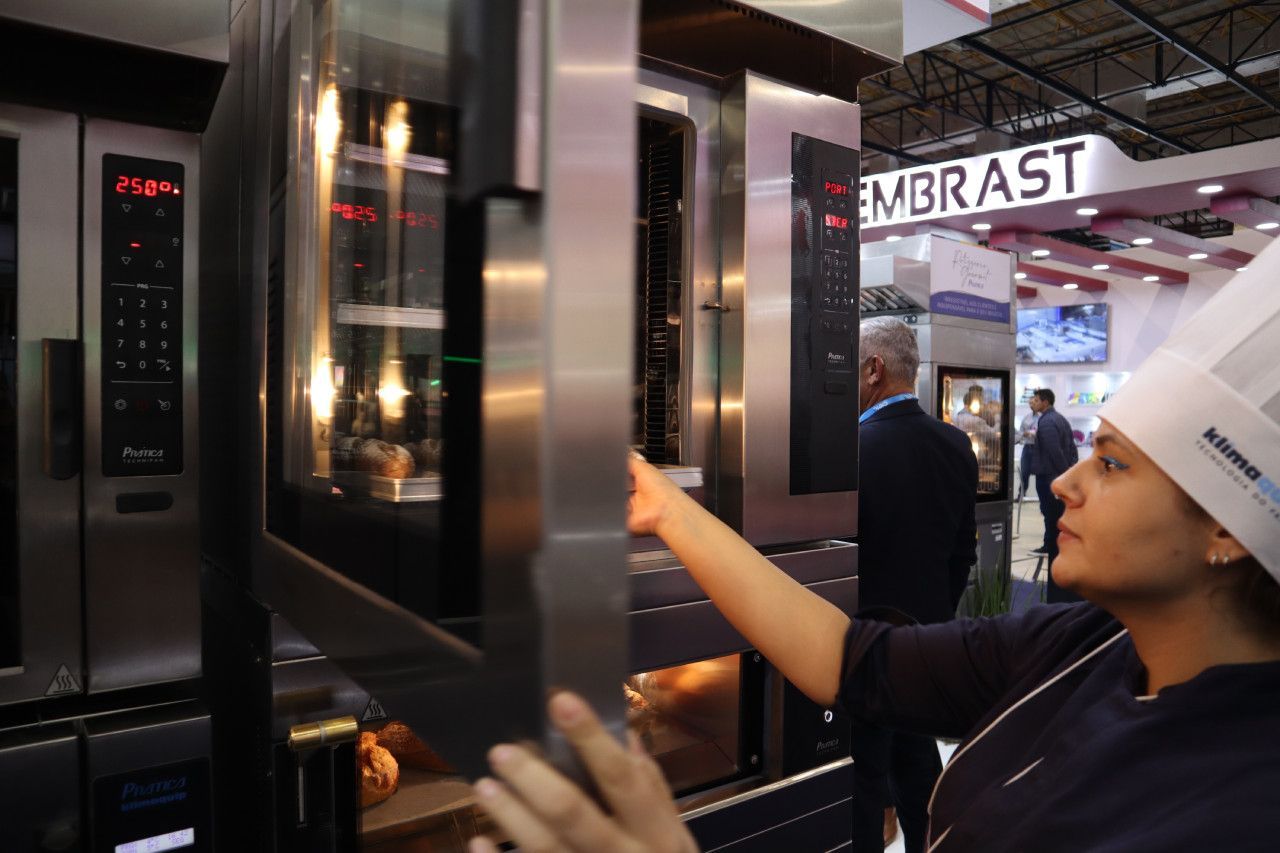 Uma mulher com chapéu de chef aponta para um forno de aço inoxidável.