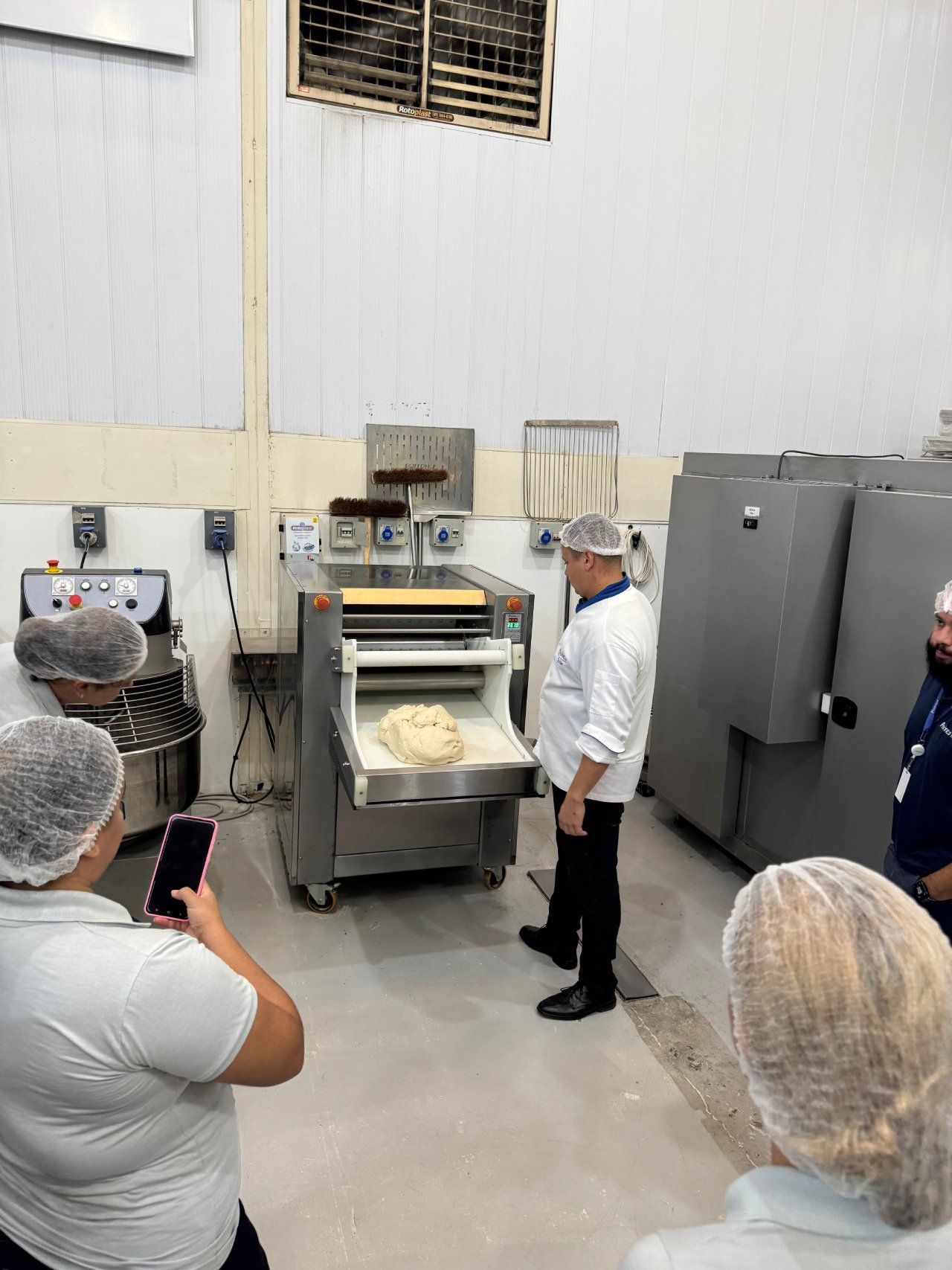 Um grupo de pessoas está em volta de uma máquina em uma padaria.