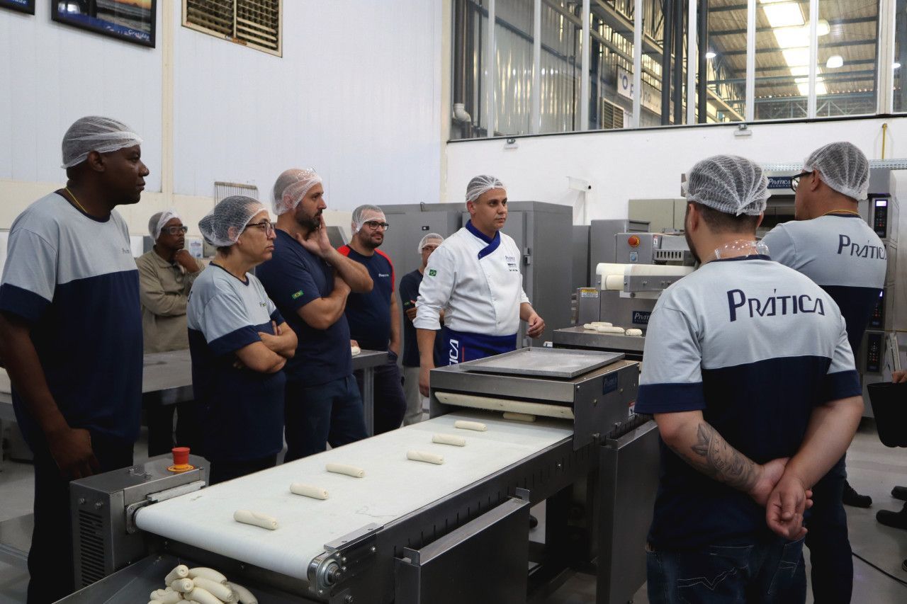 Um grupo de pessoas está em pé ao redor de uma correia transportadora em uma fábrica.