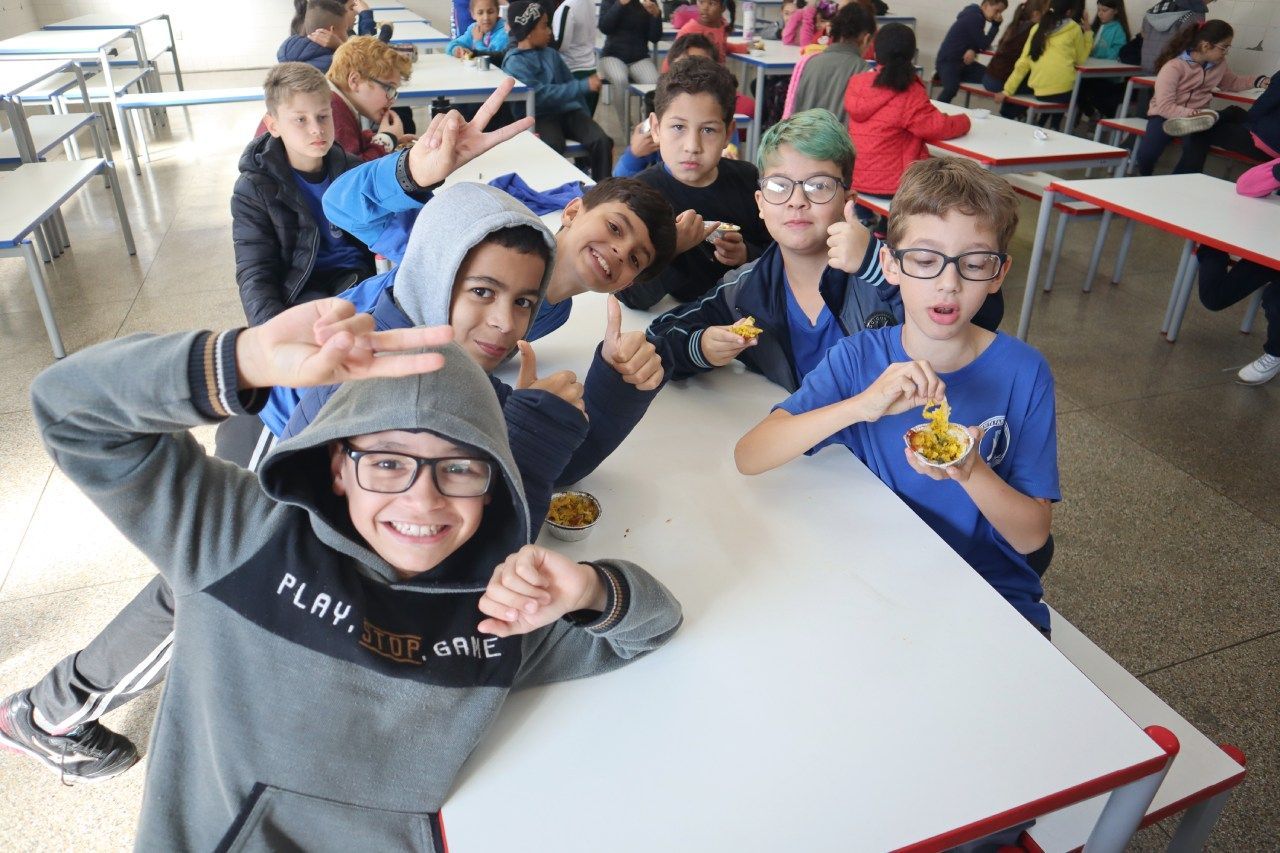 Um grupo de crianças está sentado à mesa no refeitório de uma escola.