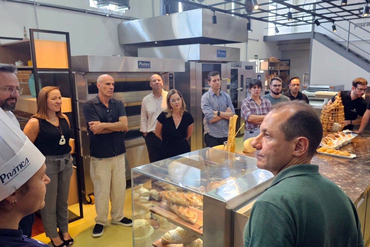 Um grupo de pessoas está em volta de uma vitrine em uma padaria.