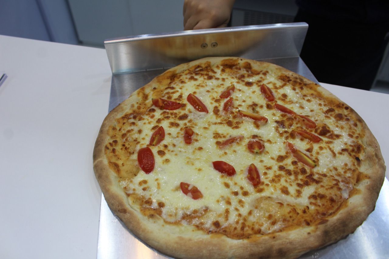 Uma pizza com queijo e tomate está sendo fatiada em uma tábua.