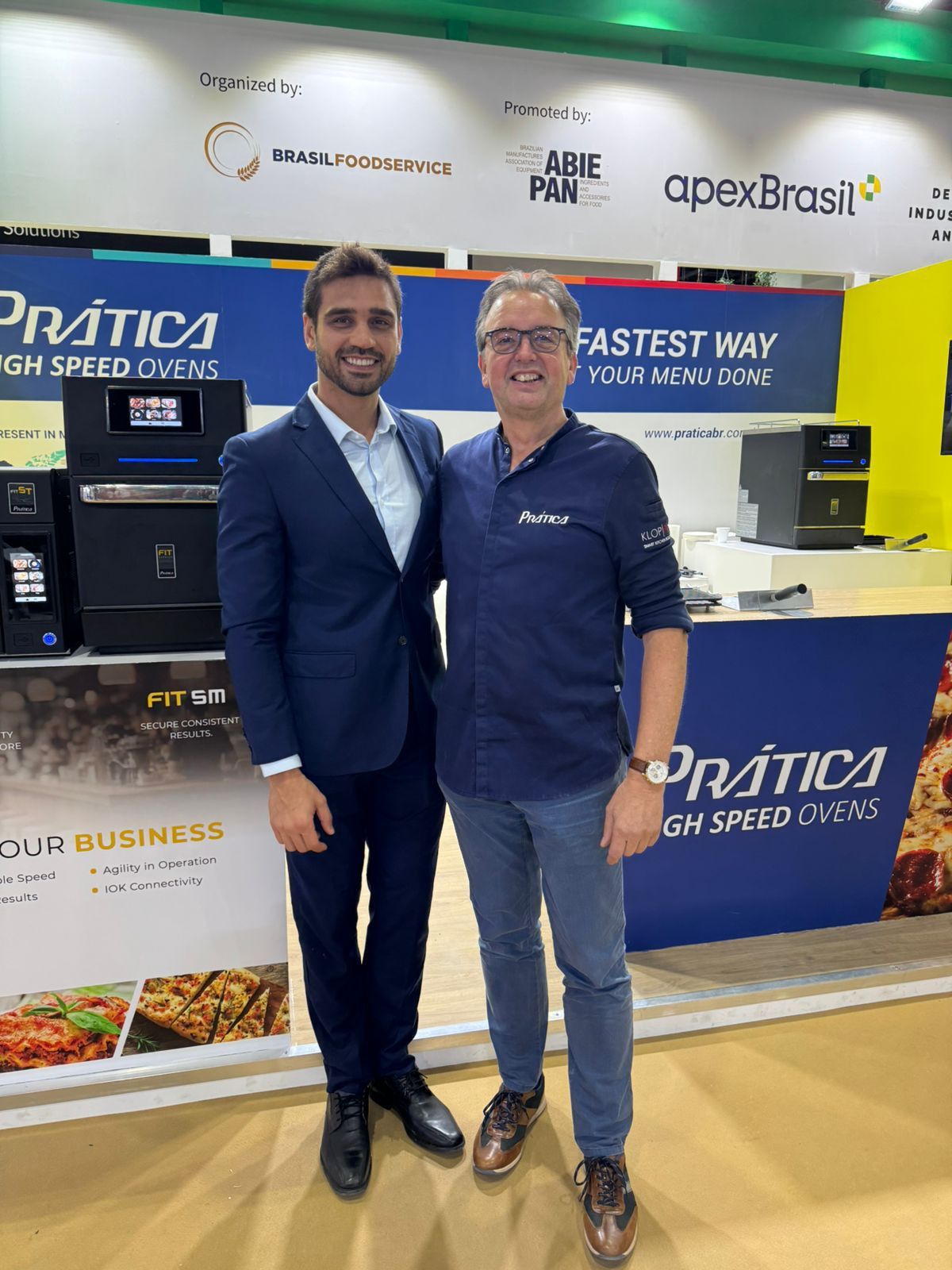 Dois homens estão parados um ao lado do outro em frente a um balcão.