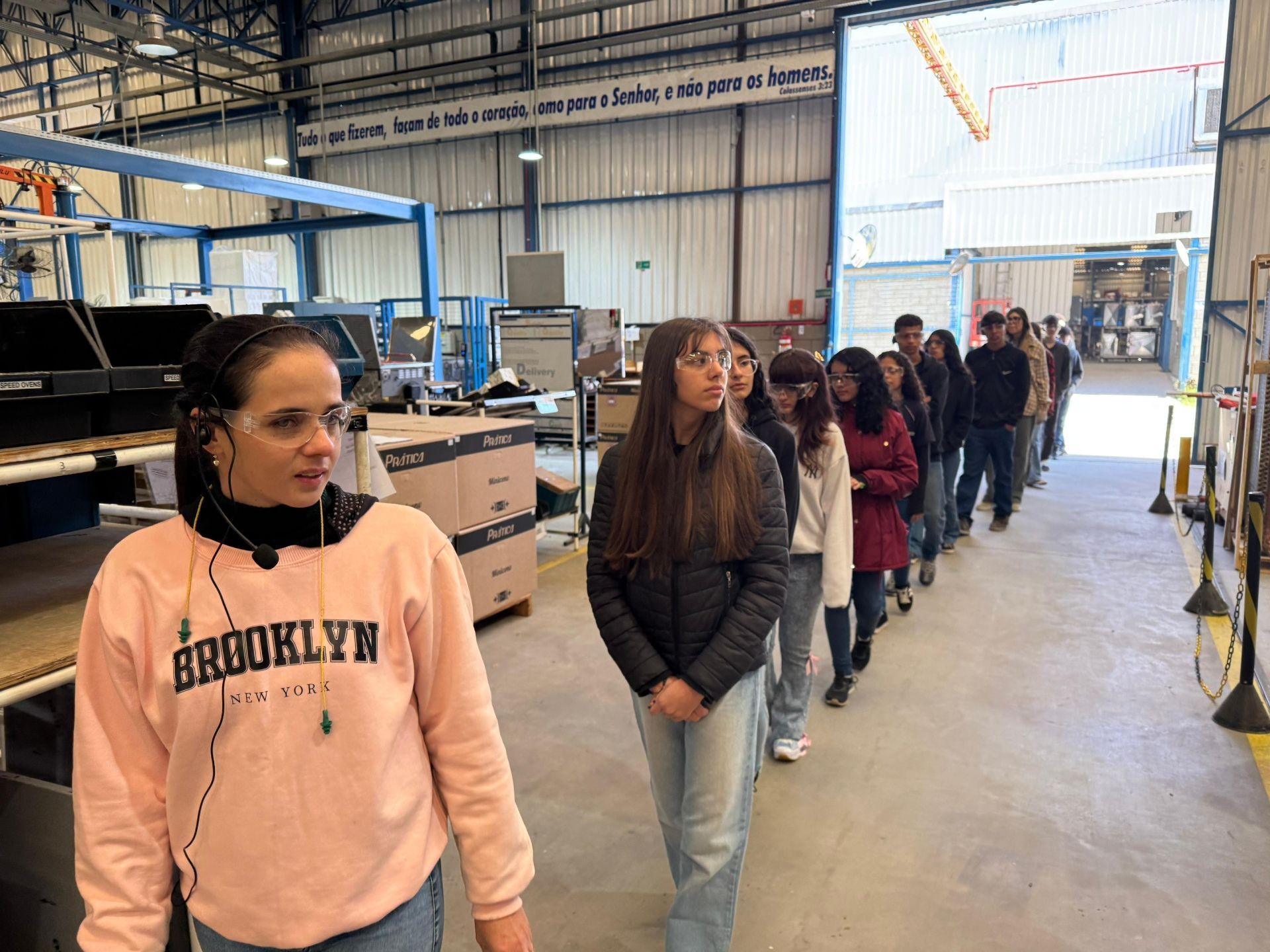Um grupo de estudantes em um passeio por uma fábrica, caminhando em fila.