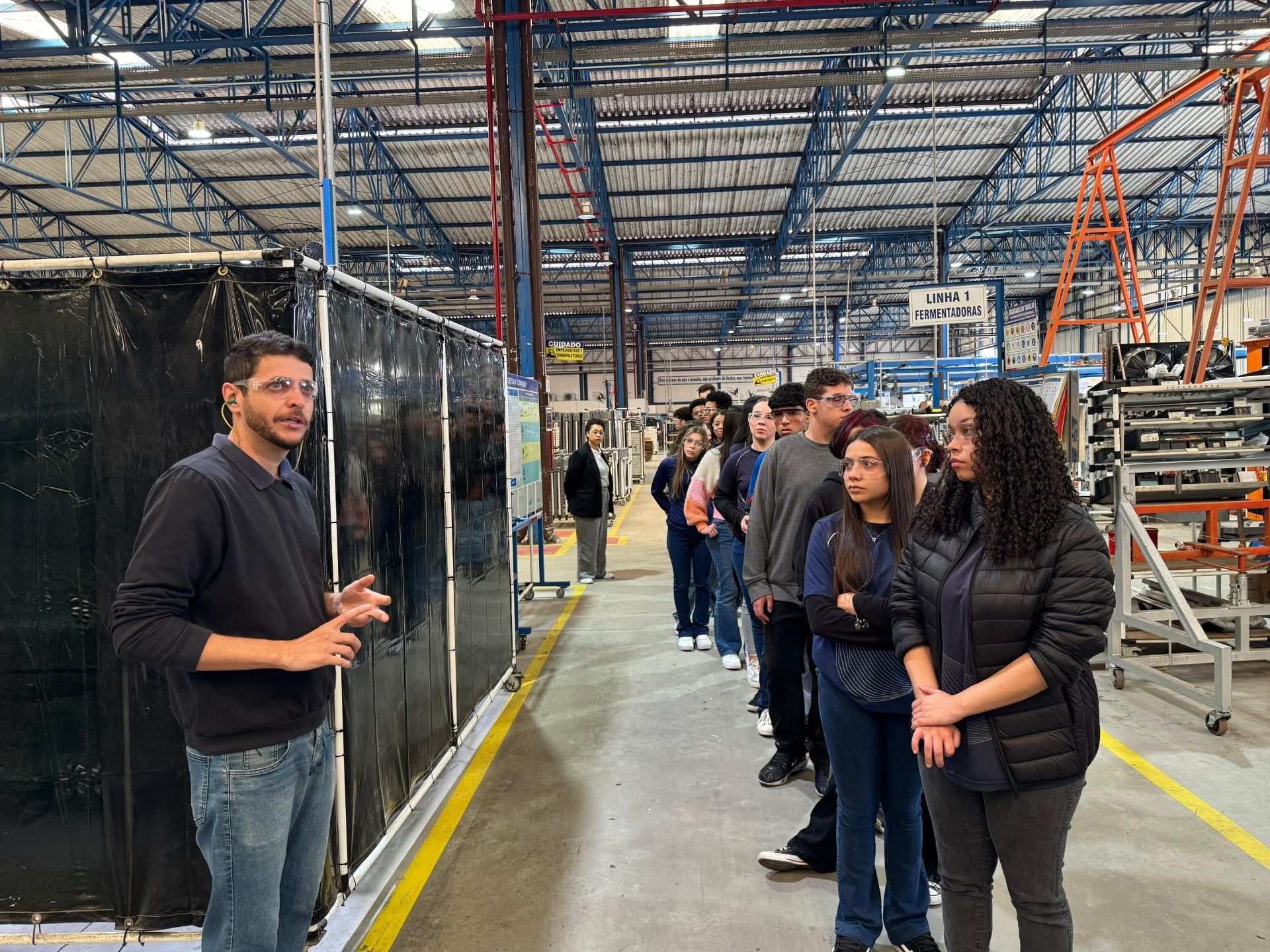 Um grupo de estudantes em um passeio por uma fábrica, ouvindo um guia.
