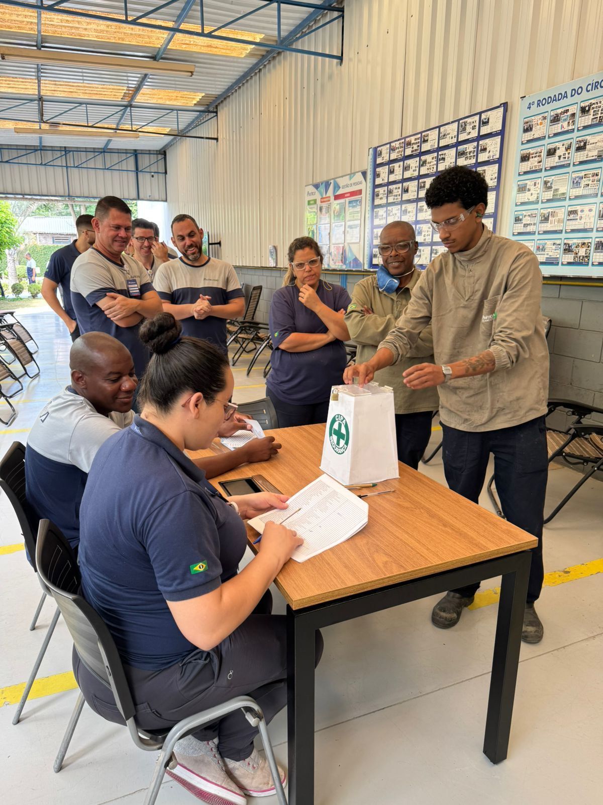 Um grupo de pessoas está sentado ao redor de uma mesa em um armazém.