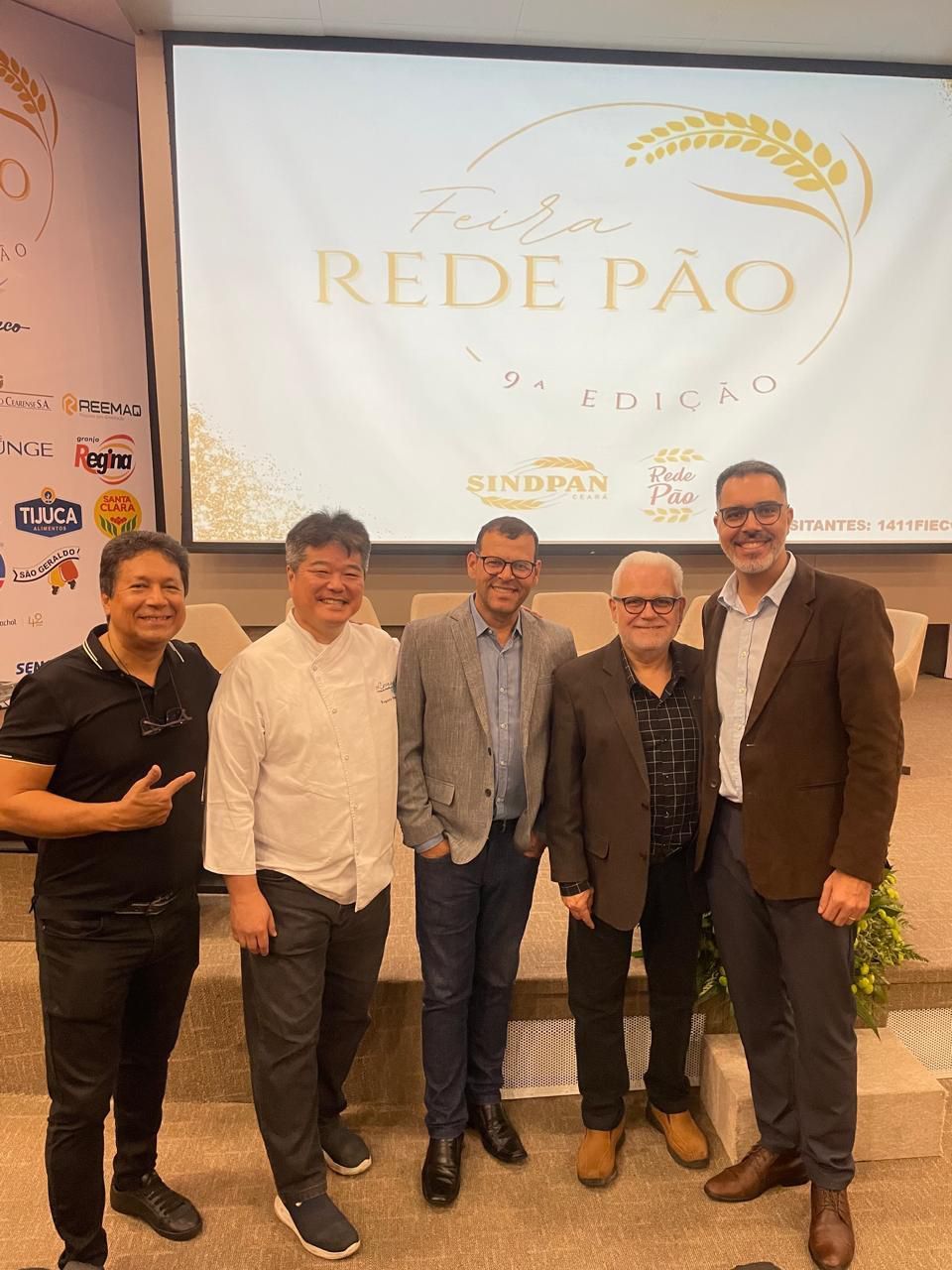 Um grupo de homens está posando para uma foto em frente a uma tela grande.