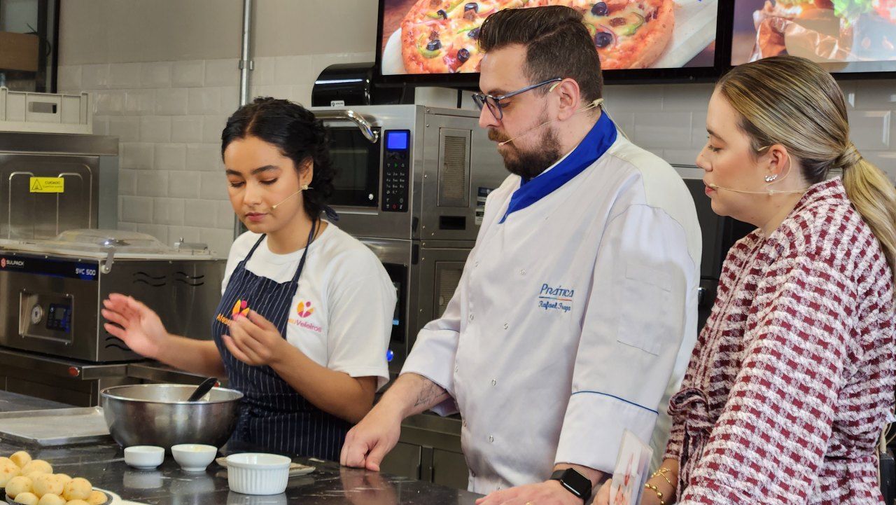 Um grupo de pessoas está em pé ao redor de uma mesa na cozinha.