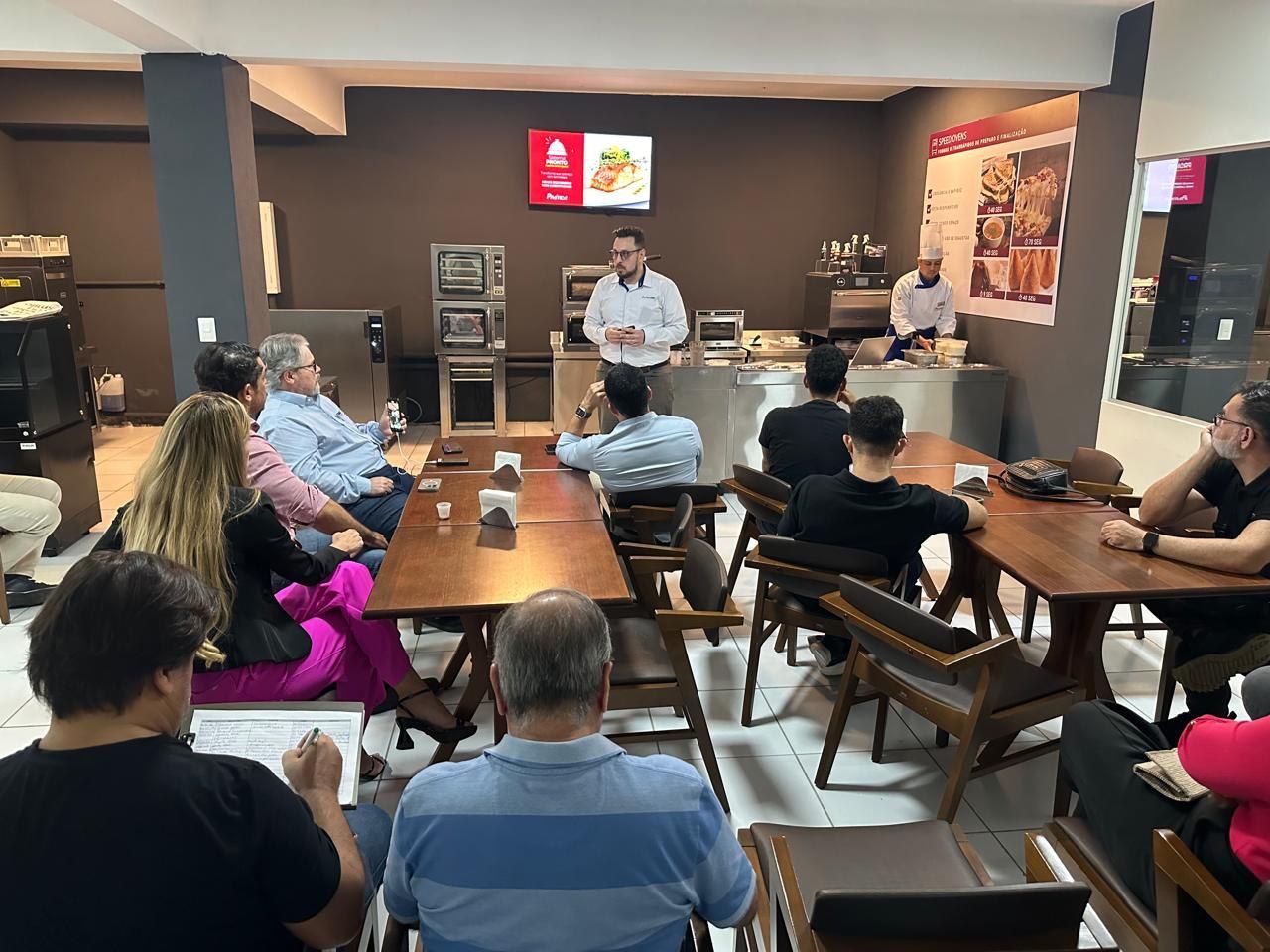 Um grupo de pessoas está sentado em mesas em uma sala.