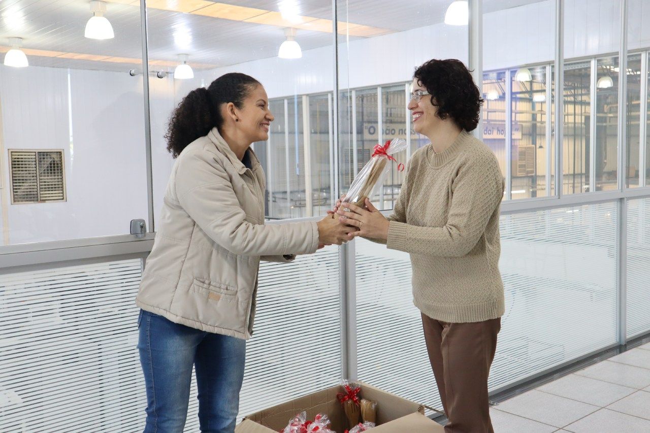 Duas mulheres estão de pé, uma ao lado da outra, em uma sala, de mãos dadas.