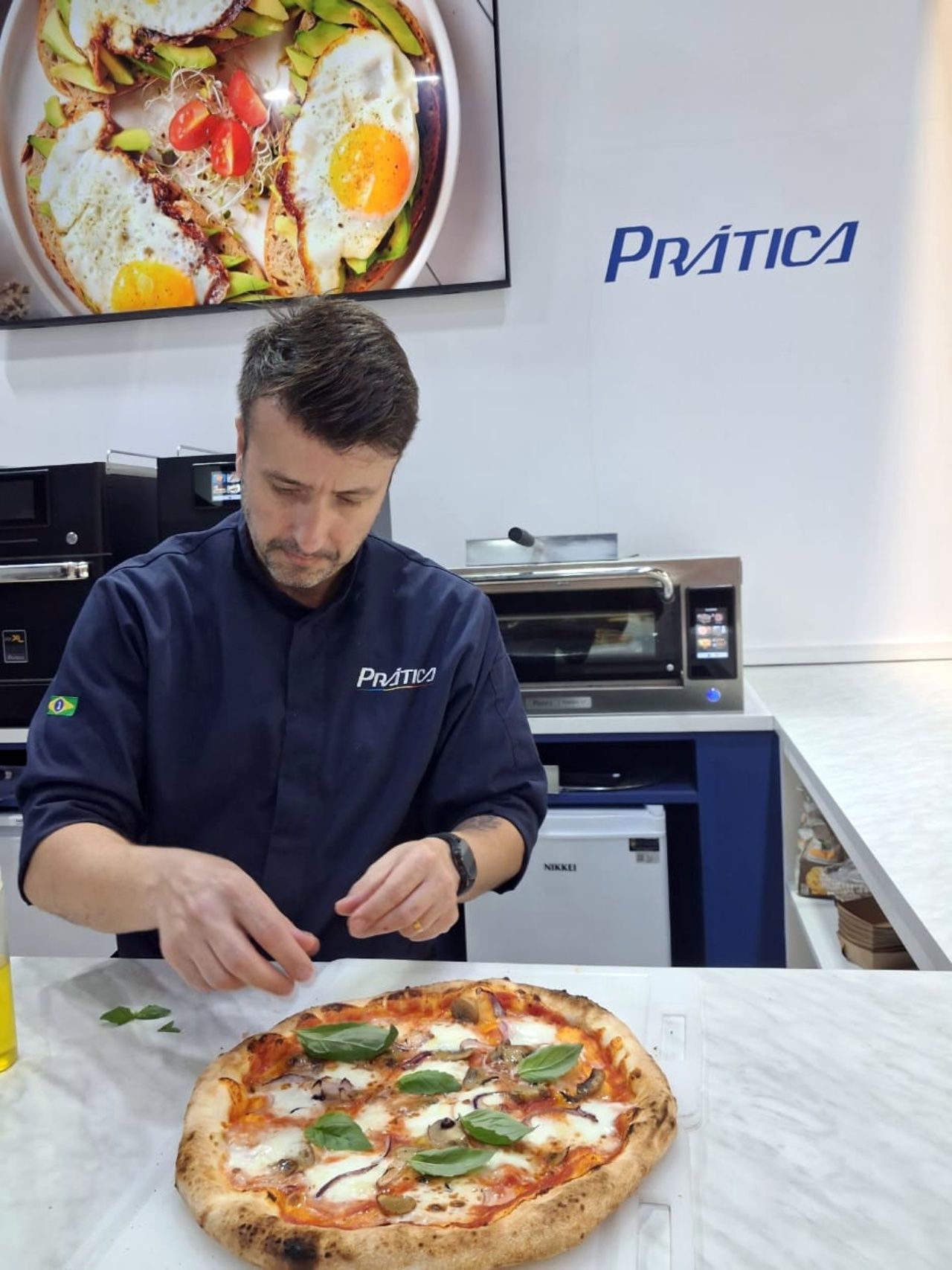 Chef colocando manjericão em uma pizza. O cenário é uma cozinha com o logotipo da Prática.