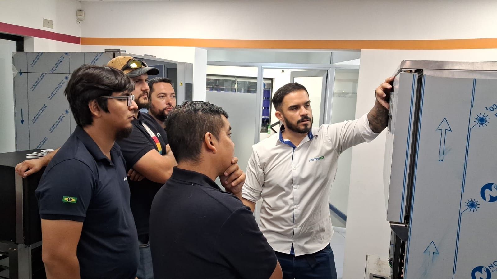 Um homem apontando para uma máquina, cercado por outros homens em um ambiente de escritório.