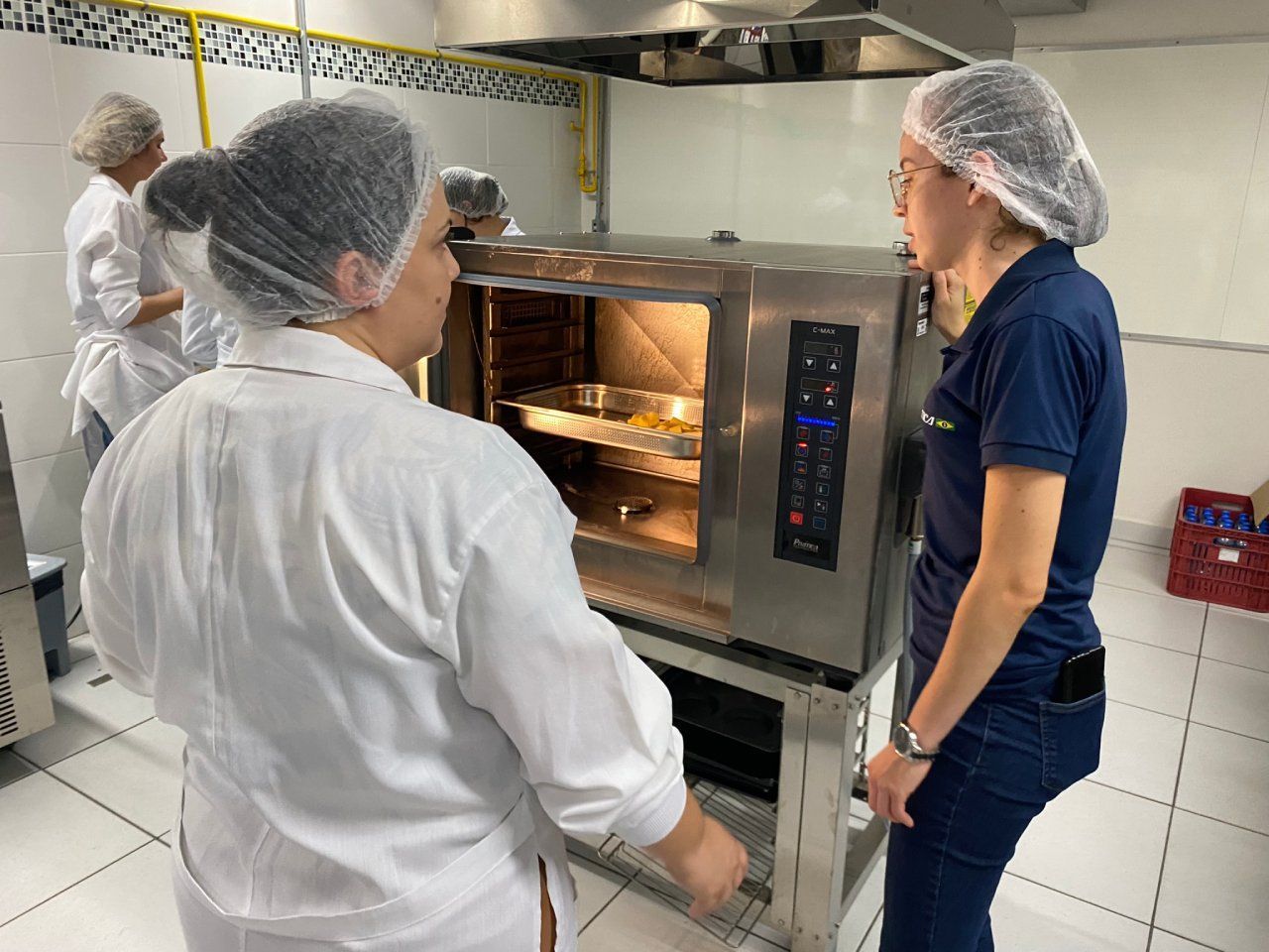 Duas mulheres estão em pé na frente de um forno na cozinha.