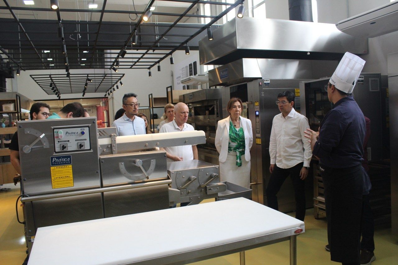 Um grupo de pessoas está em uma cozinha olhando para uma máquina.