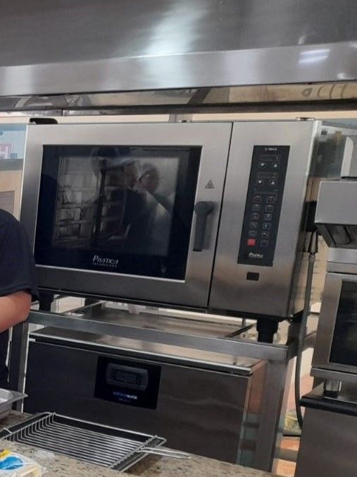 Um homem está em frente a um forno de aço inoxidável com a palavra