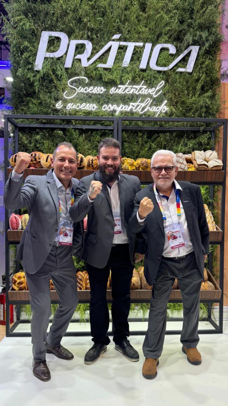 Três homens de terno estão posando para uma foto em frente a uma exposição de frutas e vegetais.