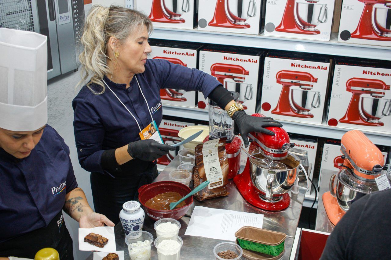 Uma mulher está parada em frente a uma batedeira vermelha KitchenAid.