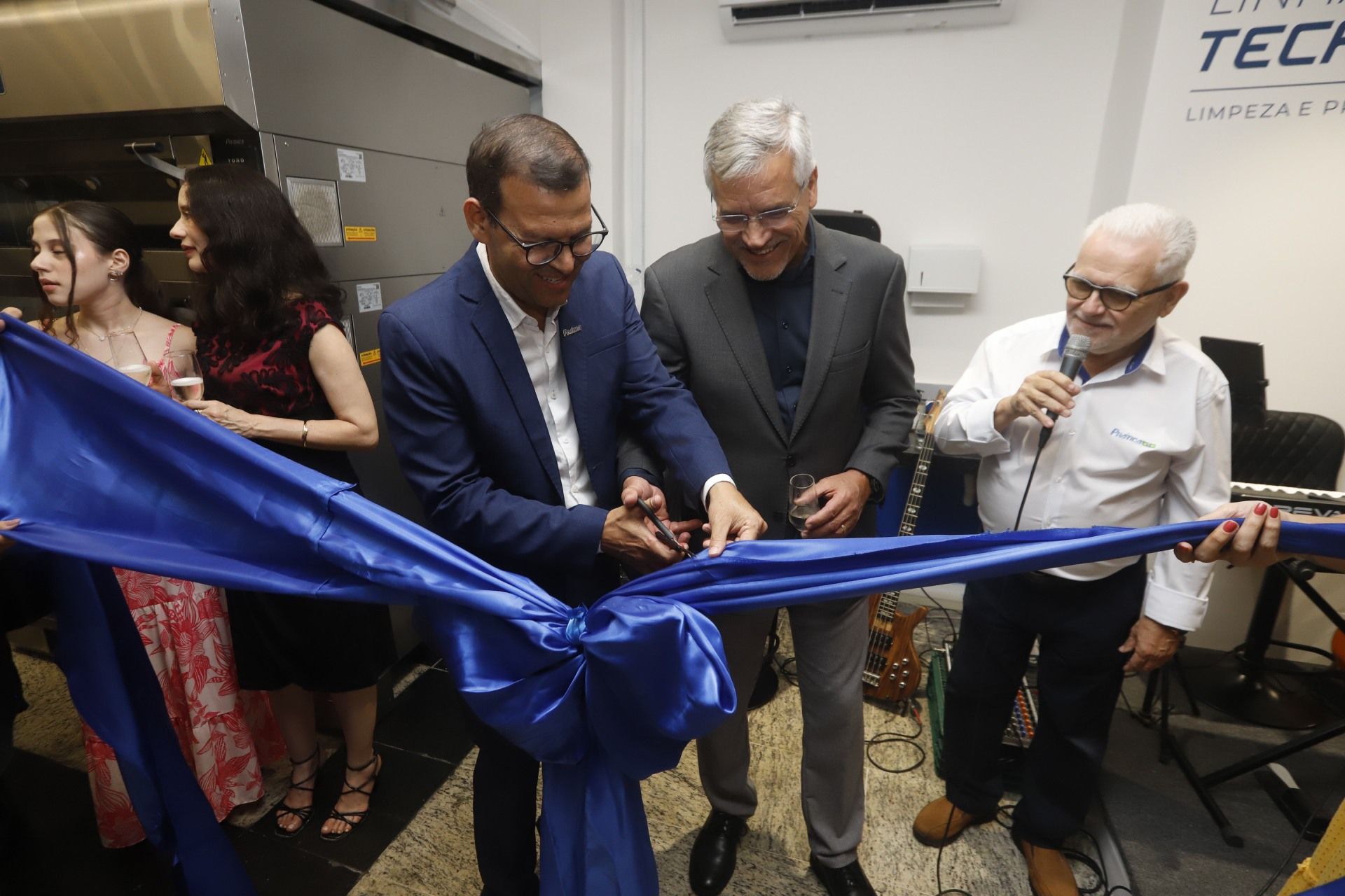 Homens cortando a fita azul em um evento com espectadores.