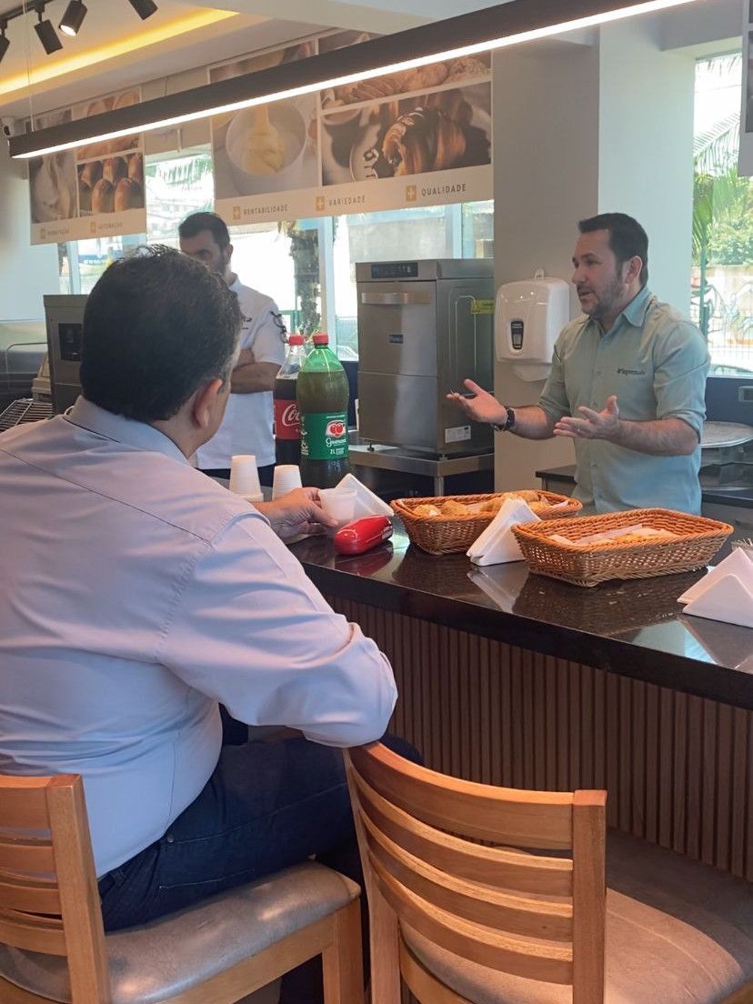 Um homem está sentado no balcão de um restaurante conversando com outro homem.