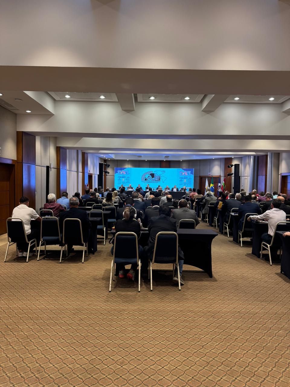 Uma grande sala cheia de pessoas sentadas em mesas e cadeiras.