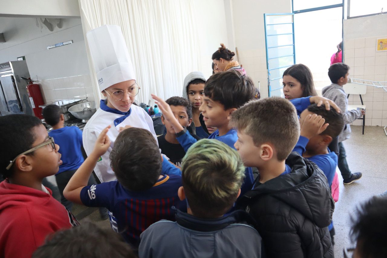 Um grupo de crianças está em volta de um chef em uma cozinha.