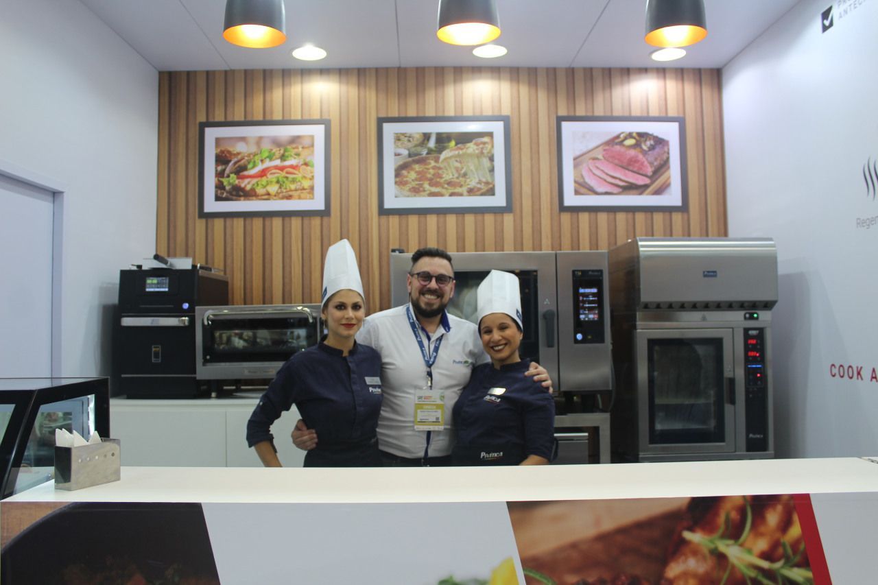 Um homem e duas mulheres posam para uma foto em uma cozinha.
