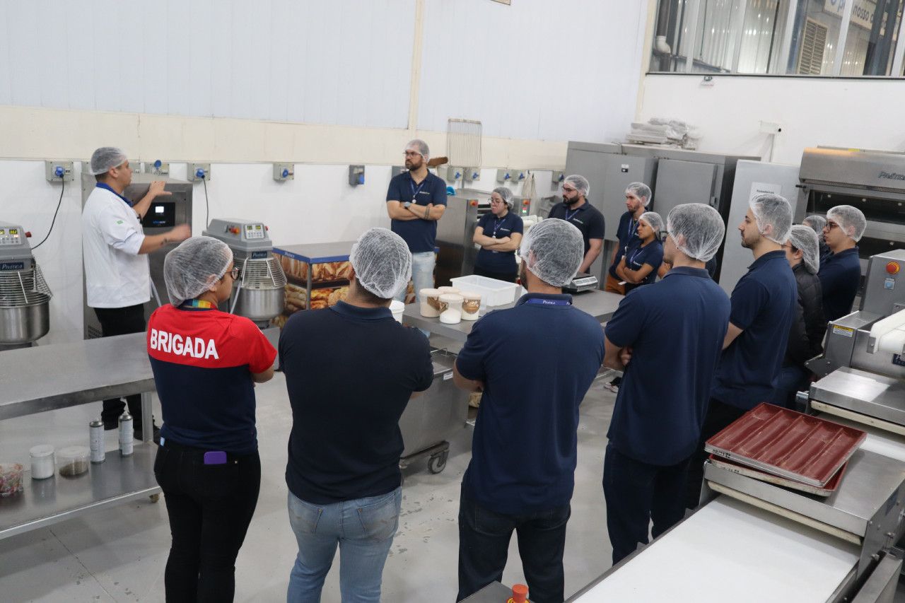 Um grupo de pessoas está em pé ao redor de uma mesa em uma padaria.