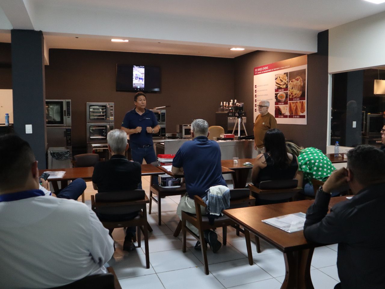 Um homem está fazendo uma apresentação para um grupo de pessoas sentadas em mesas.