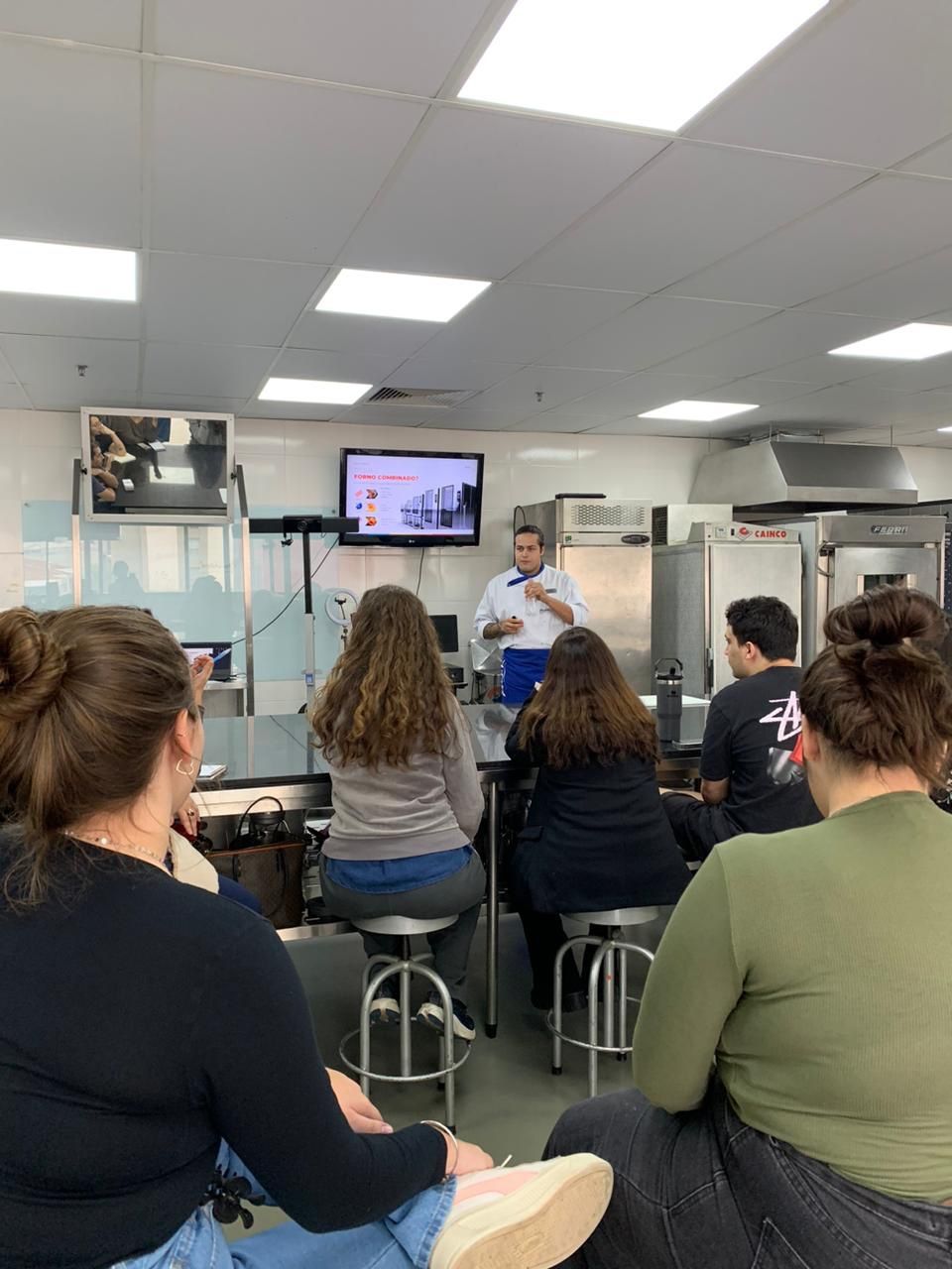 Um homem está fazendo uma apresentação para um grupo de pessoas em uma cozinha.
