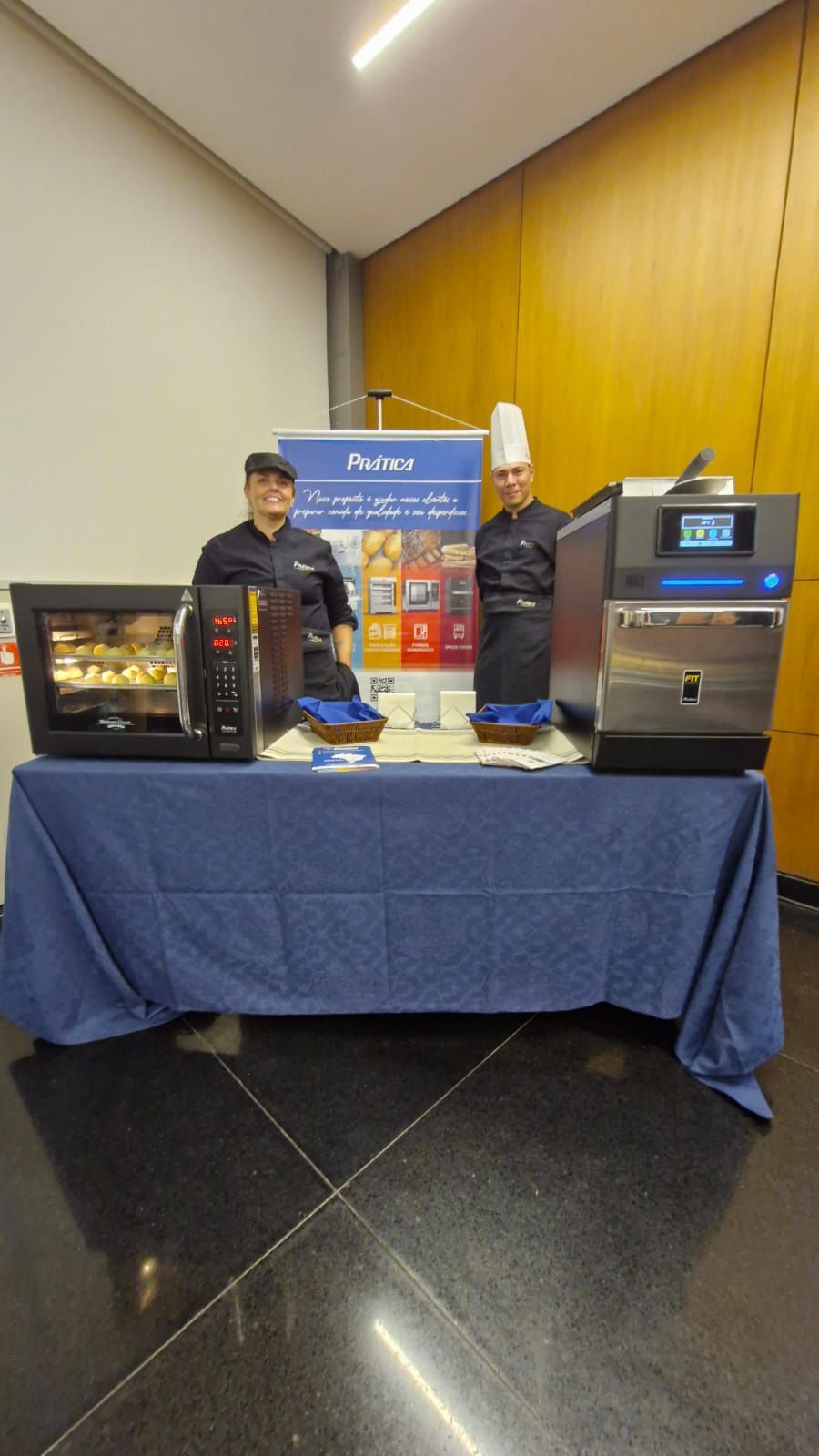 Dois homens estão de pé atrás de uma mesa com uma toalha de mesa azul.