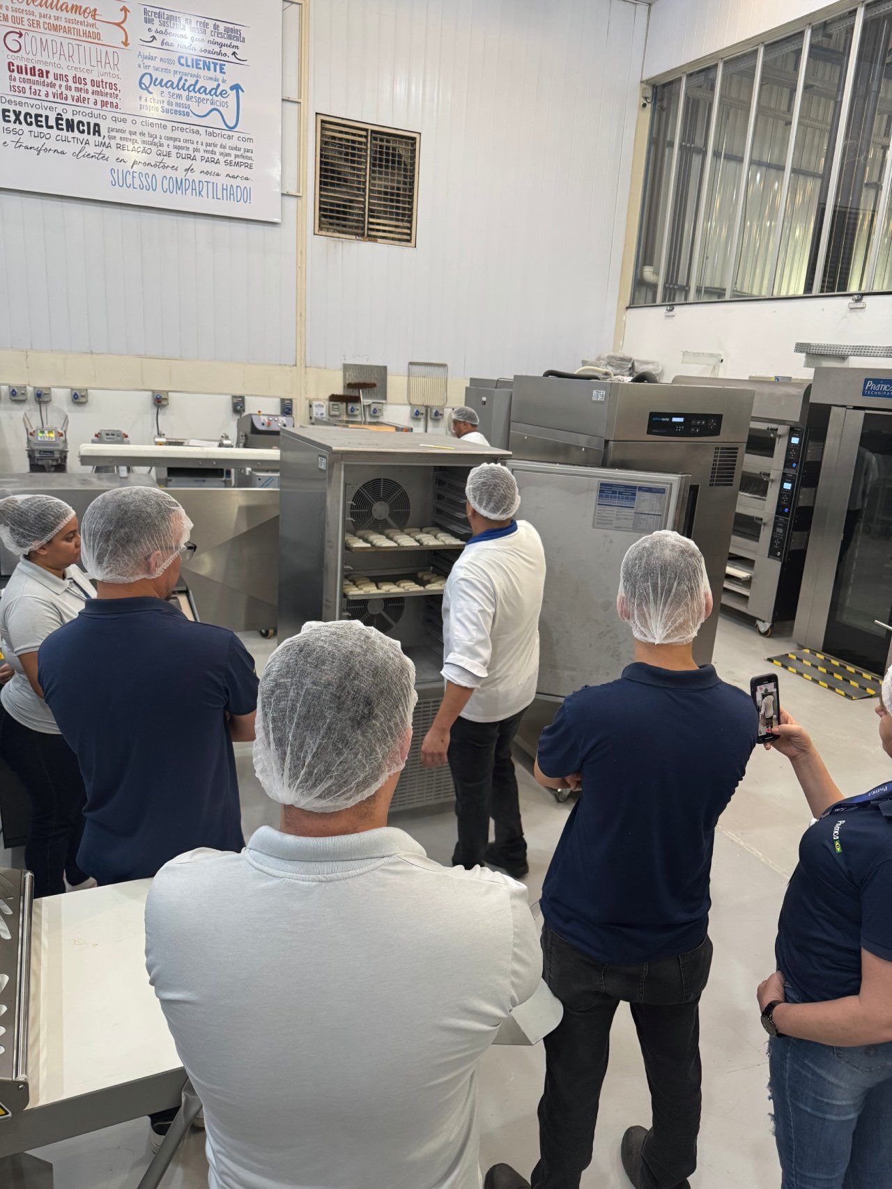 Um grupo de pessoas está em uma cozinha olhando para uma máquina.