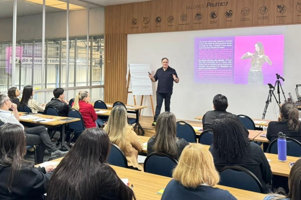 Um homem dá uma palestra para um grupo em uma sala de aula, uma apresentação na tela.